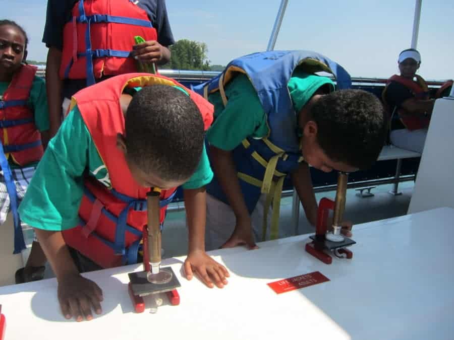 two boys on boat looking through microscope