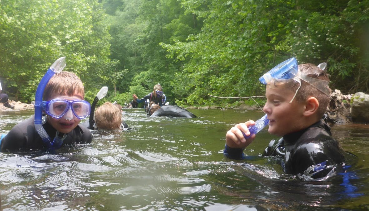 two young students swimming with snorkels and wetsuits in river