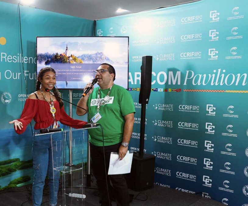 Maria Victória Pessoa and her father, Marcos Pessoa, talk about her work at the Caribbean Community Climate Change Center (CARICOM) Pavilion.