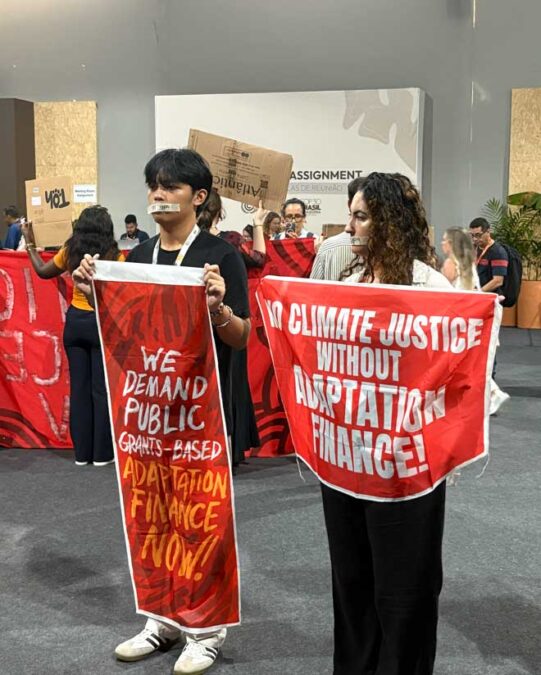Youth protestors at COP30 place tape over their mouths and hold banners in support of adaptation finance– a major cornerstone to the international negotiations at COP30.