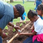mentor giving young girl seeds to plant in garden
